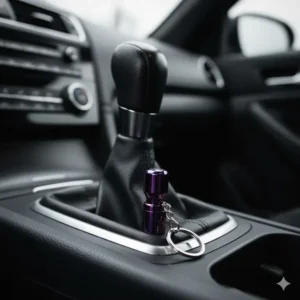 Detail shot of a miniature titanium JDM shift knob keychain next to a full-size car shifter for scale.