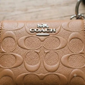 Close-up details of the stitching and metal logo on a Coach wallet key ring.
